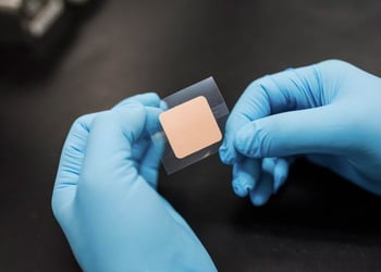 square transdermal patch being held by two gloved hands